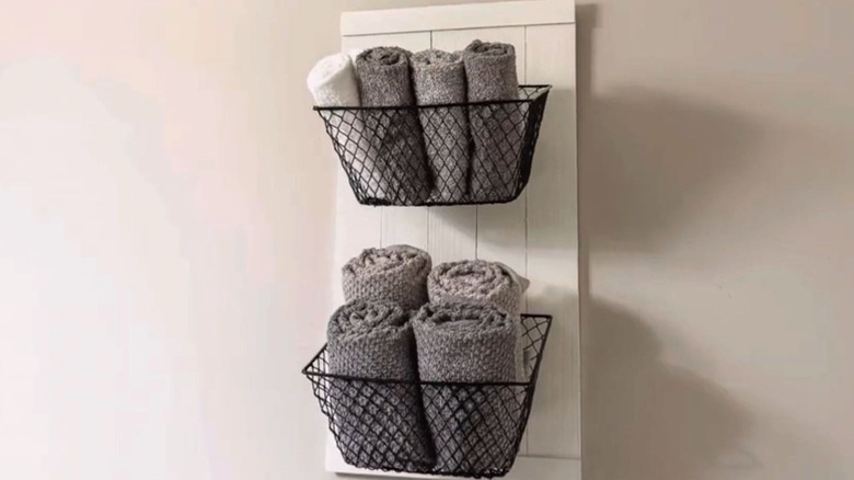 Metal baskets hanging vertically in the bathroom holding towels.