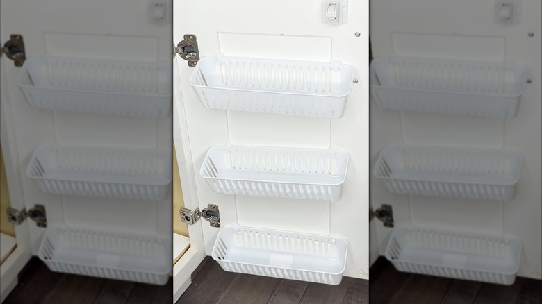 Three slotted baskets hanging on the inside of a cabinet door.