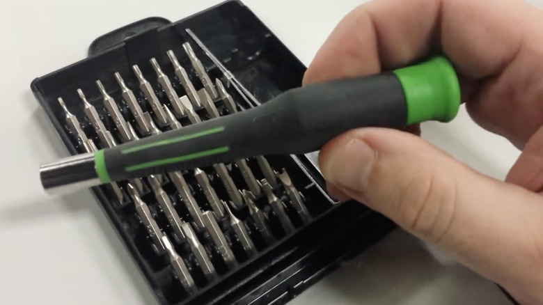 A hand holding the handle of the 32-piece Pittsburgh precision screwdriver set.