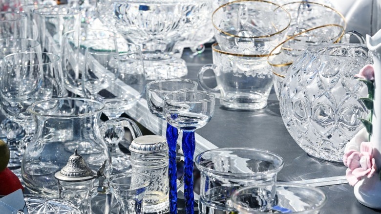 Many pieces of glassware in different shapes and sizes on a shelf in a thrift store.