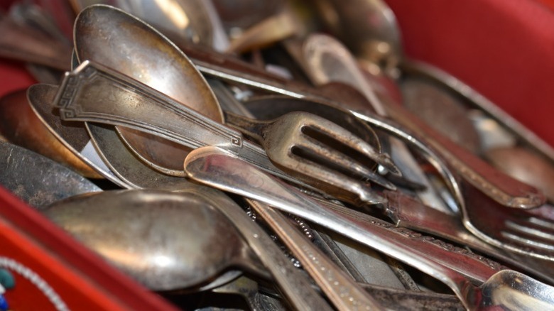 A jumble of vintage and antique silverware in a red metal box.