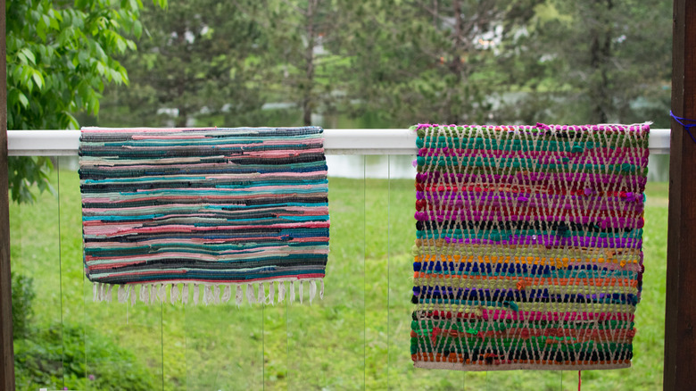 Colorful cotton rugs hanging on railing outdoors.