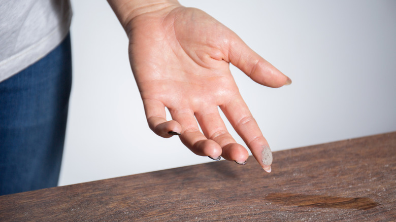 woman's hand picking up dust from wooden table