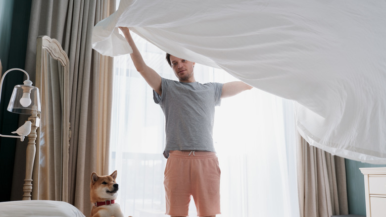 Man making bed with dog watching.