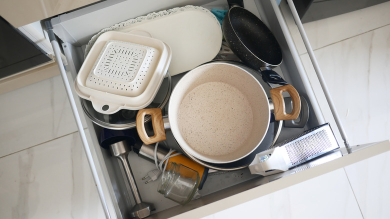 Close-up of cluttered kitchen drawer with pots, pans, and tools