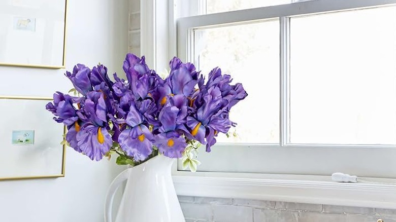 Purple artificial irises in a white vase in front of a window