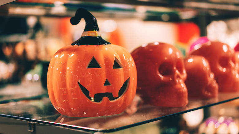 Ceramic jack-o'-lantern with witch hat on glass shelf with ceramic skulls