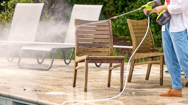 A person cleaning wooden patio furniture with Ryobi's 18V One+ 700 PSI Cordless Cold Water Electric Power Cleaner