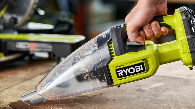 A person clearing sawdust with Ryobi's 18V One+ Cordless Multi-Surface Handheld Vacuum Kit
