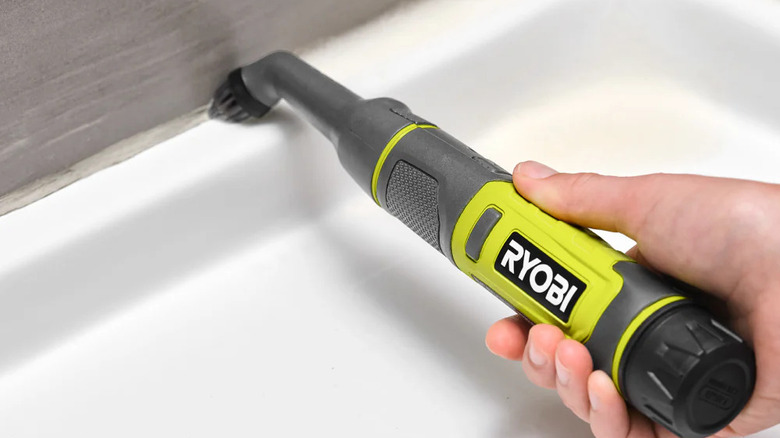 A person cleaning grout around a shower tray with Ryobi's USB Lithium Cordless Compact Detail Scrubber Kit