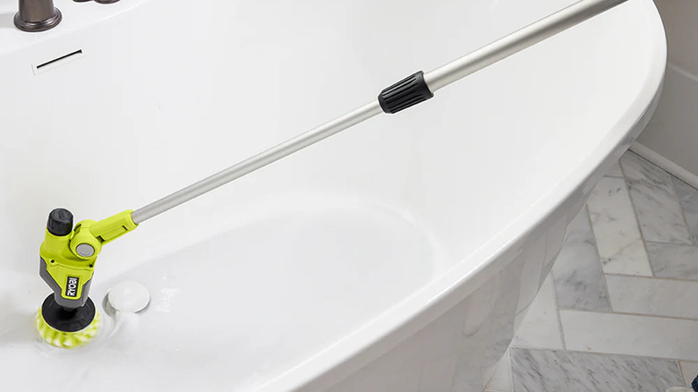 A person scrubbing a bathtub with Ryobi's USB Lithium Telescoping Power Scrubber Kit