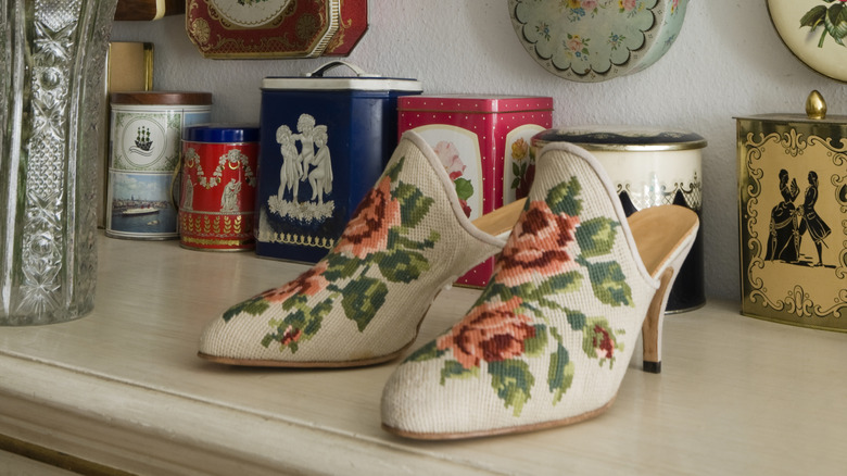 Vintage cross stitch shoes sitting in front of a display of decorative tins.
