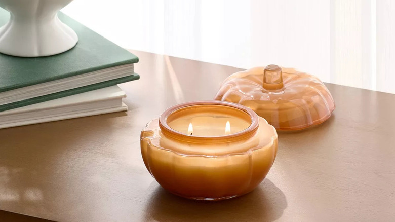 A lit pumpkin candle sitting on a table near several books