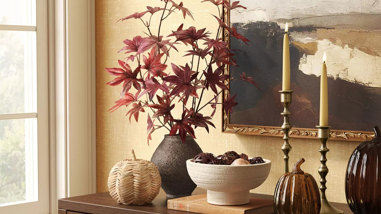 A woven pumpkin piece on a side table with fall flowers and neutral decor