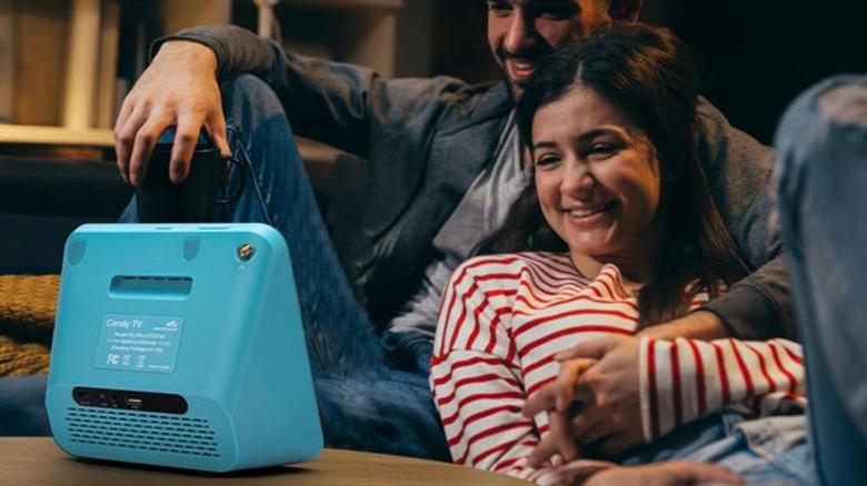 Two people lounging watching a blue portable TV.