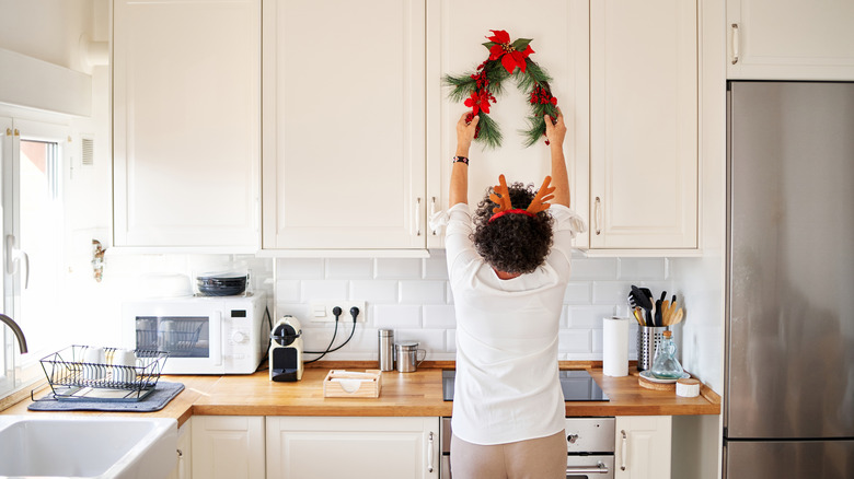 Senior woman hanging Christmas wreath on a kitchen cabinet