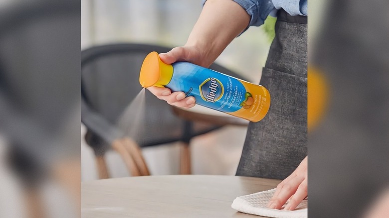 someone spraying Pledge Antibacterial Multi-Surface Cleaner on a table