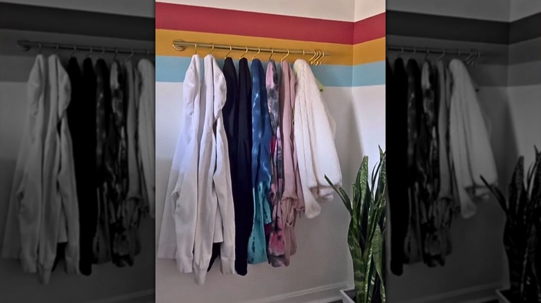 A golden towel rack with S hooks holds several jackets and coats on a colorful wall