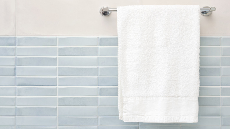 A white towel hangs on a silver towel bar in front of a tiled wall