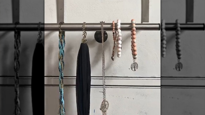 A towel rod holds a few necklaces and bracelets on a vanity