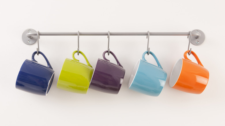 Colorful coffee mugs hang on hooks on a silver towel bar