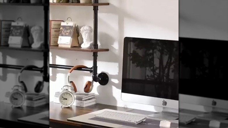 Headphones rest on a hanging bar by the computer in a home office