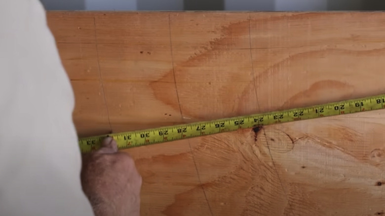 A man holding a pencil against a tape measure at an angle on a sheet of plywood with three perfect arcs drawn on it