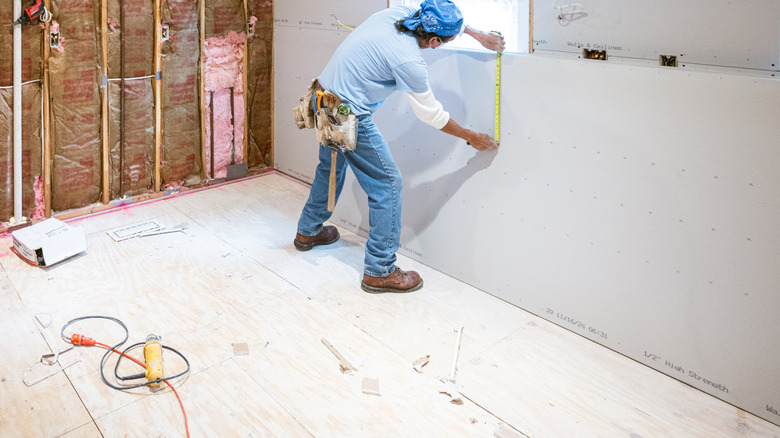 Construction worker measuring drywall from down from a window in a half constructed room
