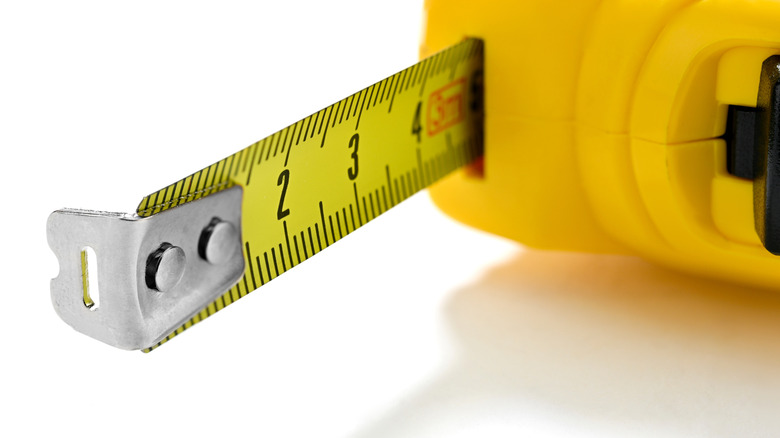 Close up of a yellow tape measure extended to four and a half inches with the metal foot showing with a hole