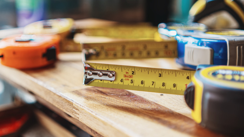 Five measuring tapes on a wooden tables at different angles with a yellow and black one at the front, slightly extended, displaying the metal foot