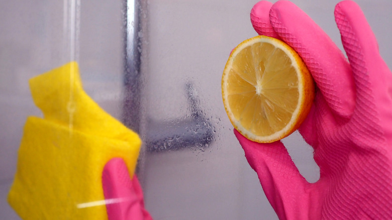 A pink gloved hand using a lemon to clean the shower