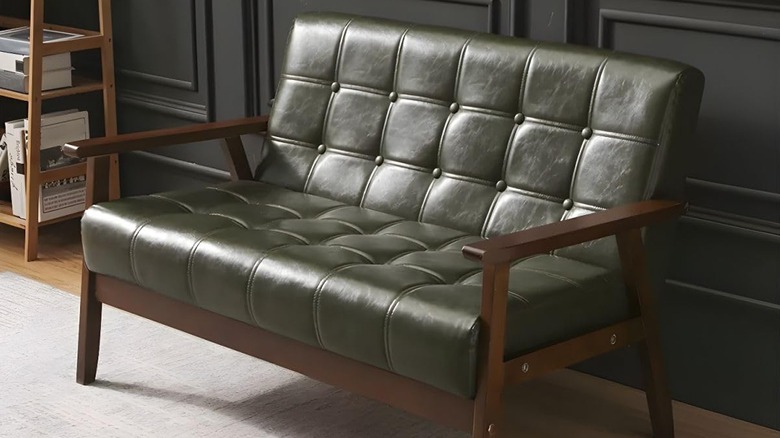 A Midcentury Modern loveseat upholstered in Army green faux leather sits  near a bookshelf
