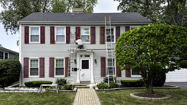 man painting shutters on home