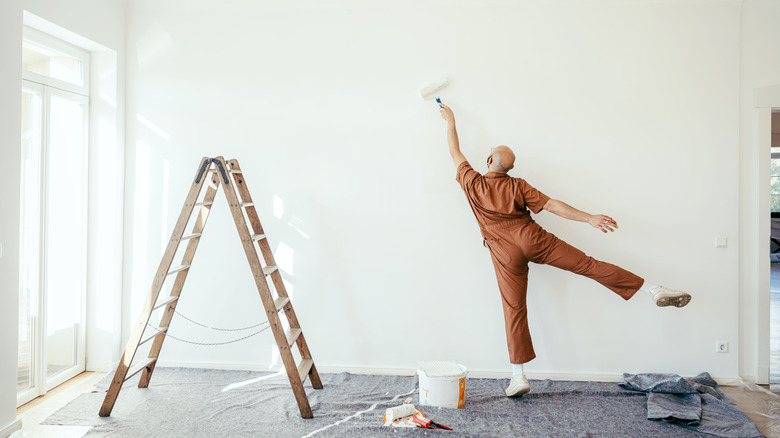 Person wearing a brown overall painting a white wall