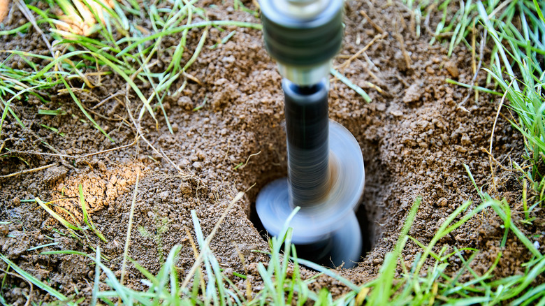 Gardener adding a hole for compost in their garden with a post hole digger