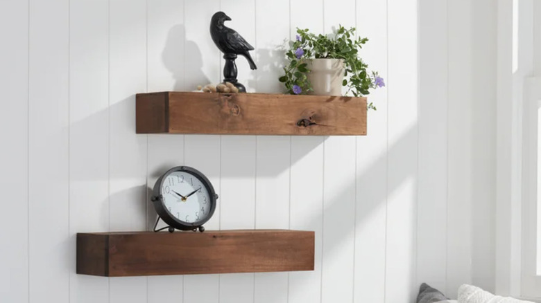 A pair of walnut floating shelves holding a clock, a bird figurine, and a plant