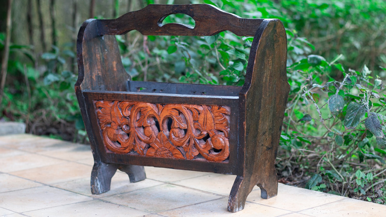 A carved magazine rack outside on a patio with plants in the background