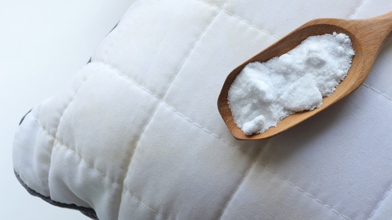 A wooden spoonful of baking soda sits on top of a white pillow