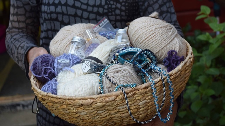 Person holding a basket full of wool, beads and other craft suppliers