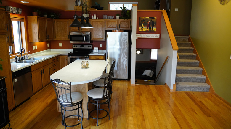 A kitchen design from the 1990s with oak cabinets, pendant lights, and an island.