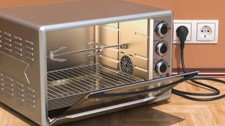 A brand new, plugged in rotisserie oven with the door open sits on a wooden countertop.