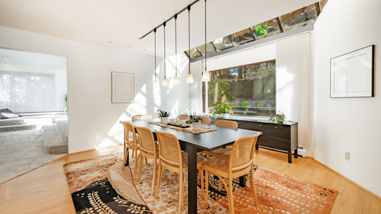 Scandinavian dining room with a simple table, a vaulted ceiling with pendant lighting, wooden chairs, and a nature-inspired rug.