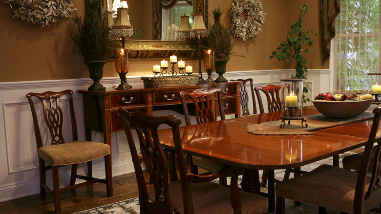 Traditional dining room with dark wood table and ornate chairs, lamps, and a large mirror.