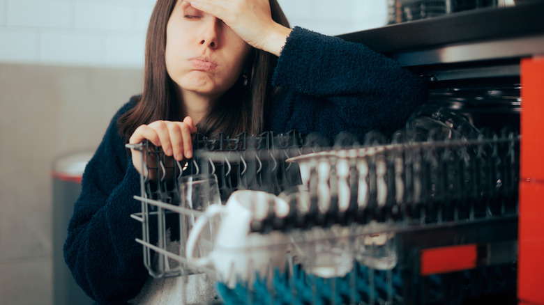 Stressed woman holding the door of a dishwasher open
