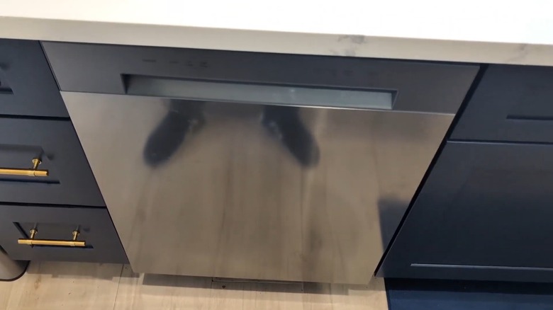 Reflection of a man's shoes in the stainless steel front of a dishwasher