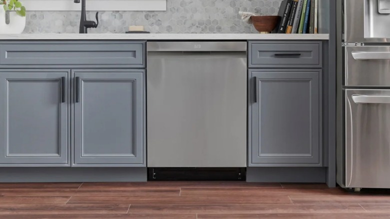 A silver-colored dishwasher nestled between blue cabinets