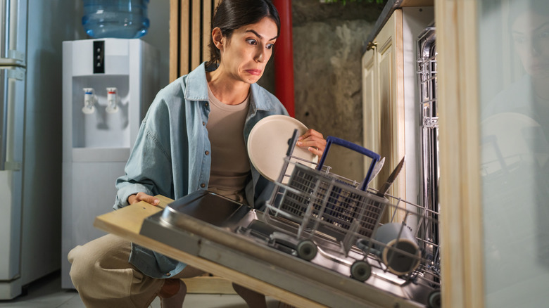 Woman trying to hold the broken door of a loaded dishwasher