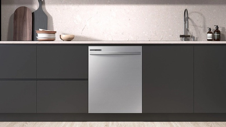 A silver-colored dishwasher installed amidst dark-colored cabinets
