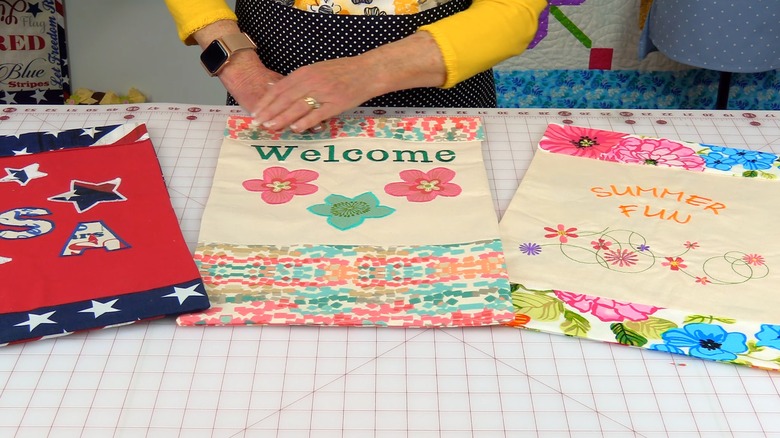 Three fabric signs lying on a sewing table with a person in the background