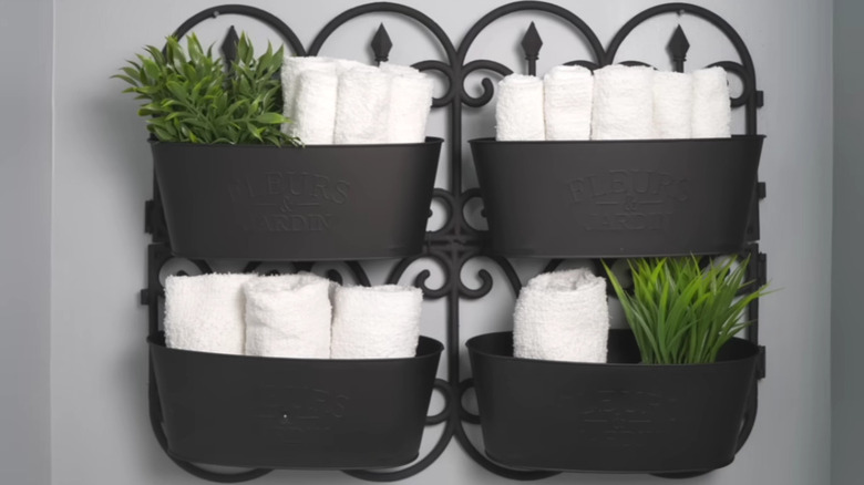 A DIY hanging bathroom organizer holding faux plants and hand towels..